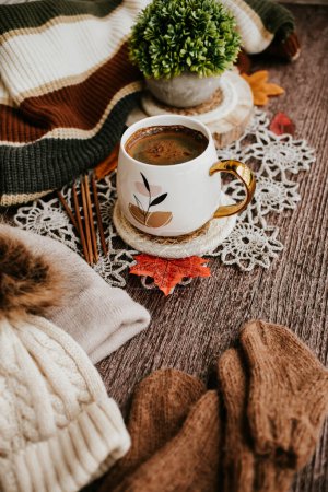 Tasse Kaffee mit Herbstblättern und gestricktem Schal auf Holzgrund