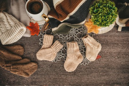 Cup of coffee with autumn leaves and knitted scarf on wooden background