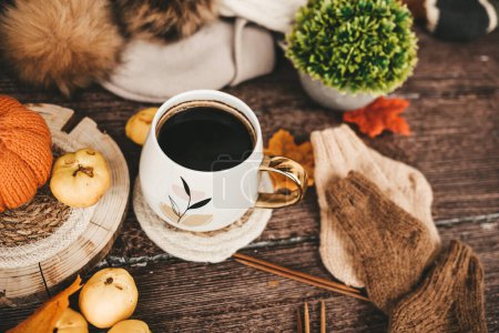 Cup of coffee with autumn leaves and knitted scarf on wooden background