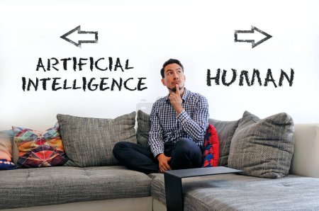 Téléchargez les photos : Homme assis sur le canapé avec les mots Intelligence artificielle et humain écrit sur le mur à côté de lui - en image libre de droit