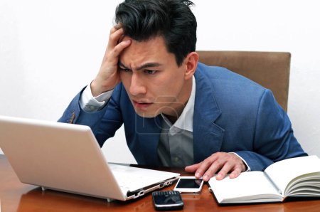 Photo for Man with worried and confused look holding hear while looking at the laptop - Royalty Free Image