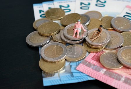 Miniature figurines of a couple relaxing and tanning on a pile of money