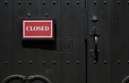 Téléchargez les photos : Une porte verrouillée en bois avec une pancarte annonçant que le bâtiment est fermé - en image libre de droit