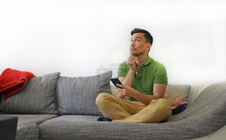 Homme avec smartphone sur canapé contemplant les options