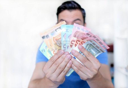 Young man holding up multiple Euro bills