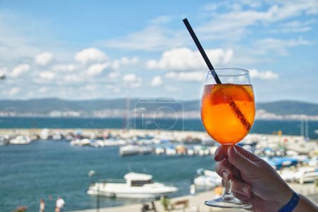 A glass of cold Aperol spritz against the backdrop of the sea coast. Vacation by the sea.