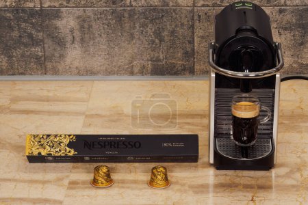 Téléchargez les photos : Thessalonique, Grèce - 17 décembre 2022 : Automatique Nespresso Machine originale pour espresso avec capsules en aluminium. Cafetière DeLonghi avec une tasse de café chaud goutte à goutte avec dosettes en métal Venezia. - en image libre de droit
