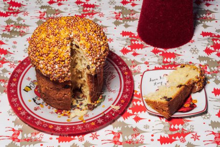 Foto de Vista superior de un pastel tradicional de Navidad panettone con una rebanada en un plato sobre una mesa con decoración festiva. - Imagen libre de derechos