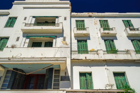 Photo for A low-rise deserted 1930s hotel with a decayed facade and green wooden window shutters under the summer blue sky. - Royalty Free Image