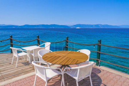 Téléchargez les photos : Café vide avec chaises et tables au bord de la mer sous un ciel bleu en été. - en image libre de droit