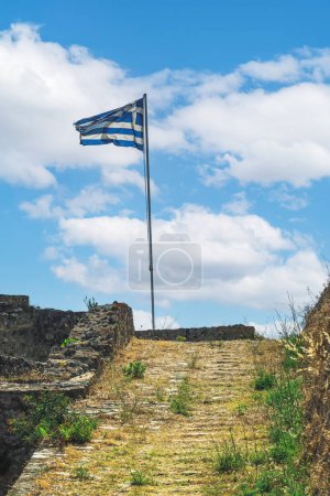 Téléchargez les photos : Drapeau grec agitant sur un must contre le ciel avec des nuages au sommet du fort d'Agia Mavra dans l'île ionienne de Lefkada, Grèce. - en image libre de droit