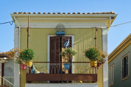 Altes buntes Hausgesicht mit Blumen auf einem eisernen Balkon und wehender griechischer Flagge auf der ionischen Insel Lefkada Griechenland.