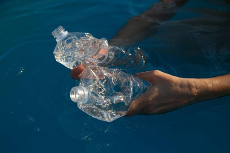Téléchargez les photos : Femmes mains ramasser une bouteille en plastique dans la mer, recyclage d'une journée à la plage - en image libre de droit