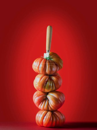 Téléchargez les photos : Gros plan sur les tomates mûres placées l'une sur l'autre avec un couteau créant une tour parfaitement équilibrée. Fond rouge. Tomates bifteck. - en image libre de droit