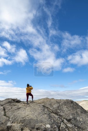 Photo for Girl captures the beauty of the Sierra de las Nieves with her cell phone, standing on prominent rock. - Royalty Free Image