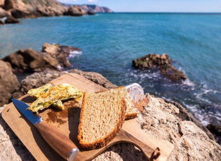Omelet on wooden bread board. In the background rocks on the seashore. focus in the foreground. Horizontal view