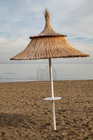 A straw umbrella in the foreground on a beach at sunset, calm and serene environment without people.