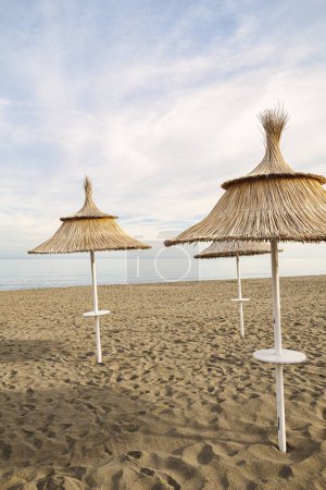Drei reetgedeckte Sonnenschirme am Strand bei Sonnenuntergang, ruhige und ruhige Umgebung ohne Menschen.