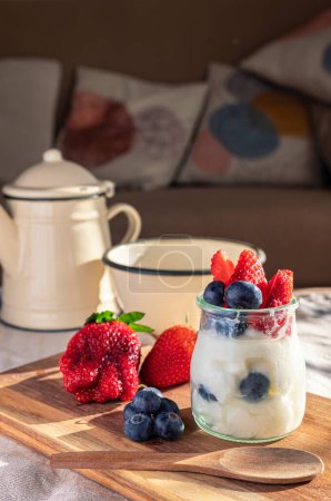 Gesundes Frühstück in der Lounge. Joghurt, Erdbeeren, Blaubeeren und Milch. Natürliches Licht aus dem Fenster