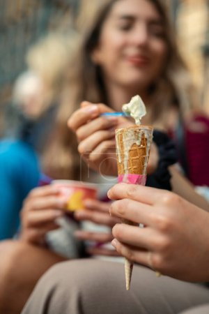 Ice cream cone in the background out of focus a Caucasian girl sitting on a staircase eating ice cream and chatting with smiling faces