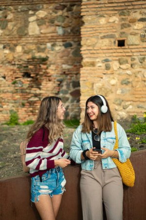 Zwei lächelnde kaukasische Mädchen teilen Musik mit Helmen und plaudern