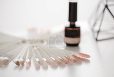 Photo for Gel lacquer bottle standing at table. Close up view of black bottle of nail polish standing at the white table at the nail salon near nude samples. Beauty routine concept, still life - Royalty Free Image