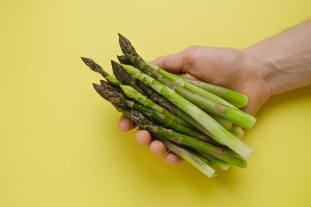 Photo for Fresh green asparagus in hand on yellow background, top view. copy space. Healthy food for balanced diet. - Royalty Free Image