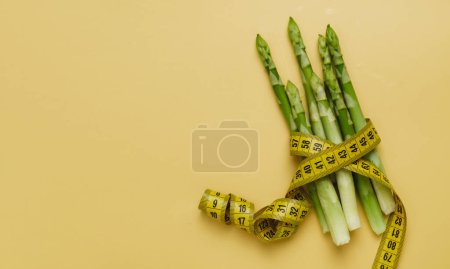 Foto de Espárragos y cinta métrica aislados de color amarillo. Alimento nutritivo equilibrado y dietético para adelgazar - Imagen libre de derechos