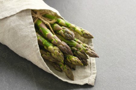 Photo for Bunch of fresh asparagus on grey table wrapped in linen towel - Royalty Free Image