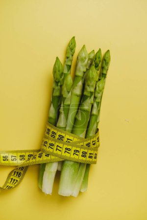 Photo for Asparagus and measuring tape isolated yellow. Diet and balanced nutrition food for weight loss concept - Royalty Free Image
