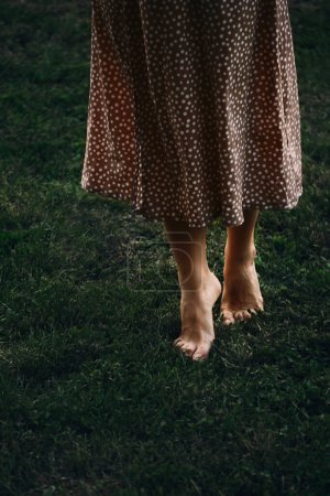 Foto de Las piernas de la mujer punta de los pies descalzos en la hierba verde oscuro. Caminando al atardecer sobre césped fresco. Libertad y relajación, conexión con la naturaleza. Tecla baja, primer plano - Imagen libre de derechos