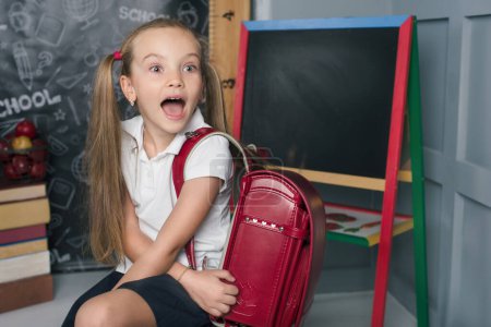Photo for School child in a classroom with chalkboard. Copy space. girl with emotions and backpack. BACK TO SCHOOL concept - Royalty Free Image