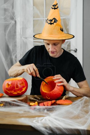 Téléchargez les photos : Homme courbant jac o lanten citrouille d'Halloween à la maison. Se préparer pour les vacances, - en image libre de droit