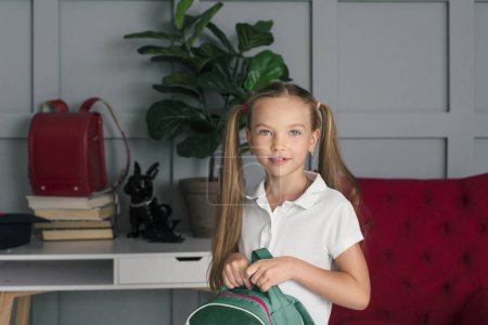 Photo for Happy schoolchild in the classroom with big backpack and positive emotions. Excieted and ready to study girl - Royalty Free Image