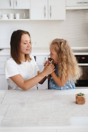 Photo for Child is having sweet snack on the kitchen. Happy toddler kid having tasty candy with mother at home. Caucasian blonde family - Royalty Free Image