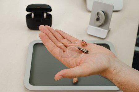 Foto de Audífonos modernos en miniatura. Audífonos invisibles pequeños y discretos en las manos. Primer plano del paciente. clínica de rehabilitación auditiva - Imagen libre de derechos
