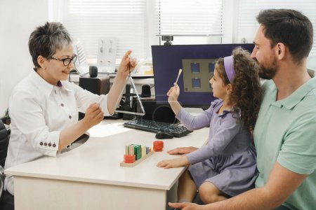 Photo for Speech therapist working with child who has hearing problems. Rehabilitation teacher of the deaf consulting father with daughter speech therapist working with child who has hearing problems - Royalty Free Image