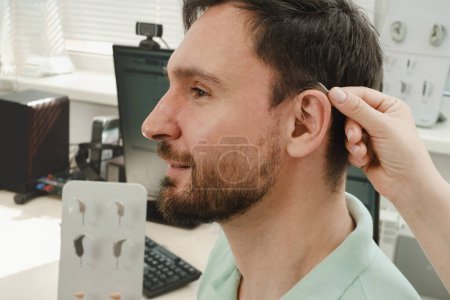 Photo for Man trying modern compact hearing aids. Closeup of patient ear. Hearing rehabilitation clinic selecting digital device for middle age deaf people. - Royalty Free Image