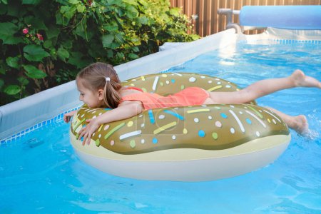 Glückliches Vorschulmädchen im Freibad auf aufblasbarem Ring. Kind genießt die Sommerzeit beim Schwimmen im Hinterhof. Kinder, die Spaß im Wasser haben, Aktivitäten für Erholung und Gesundheit. Lustiges Gesicht