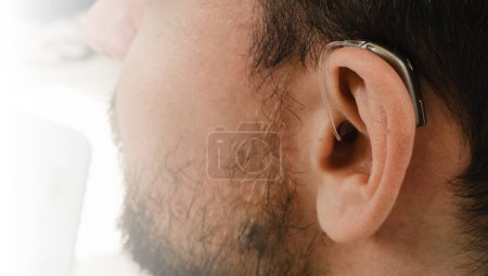 Foto de Hombre probando audífonos compactos modernos. Primer plano del oído paciente. Clínica de rehabilitación auditiva seleccionando dispositivo digital para personas sordas de mediana edad. - Imagen libre de derechos
