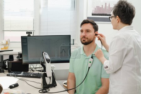 Photo for Man has appointment at clinic, checking hearing. Doctor audiologist consulting at hearing rehabilitation clinic to select digital device for middle age man. Doctor consulting patient - Royalty Free Image