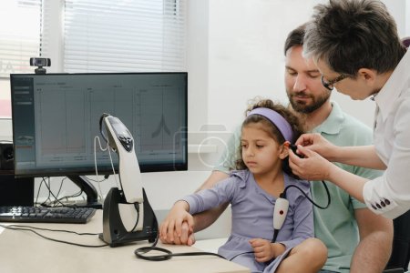 Child hearing test. Doctor audiologist consulting father of girl ear and assess disorder of hearing using screening, diagnostic technology