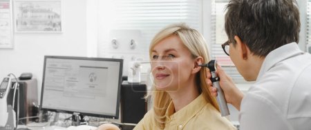 Patientin beim Hörtest beim Hals-Nasen-Ohren-Arzt. Anhörungsprüfung für Frauen. HNO-Arzt untersucht reifes Frauenohr mit Otoskop oder Auriskop in medizinischer Klinik