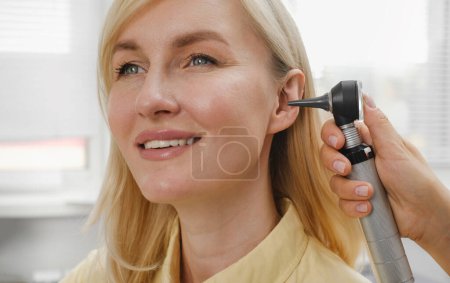 Photo for Woman patient having check-up of hearing at doctor otolaryngologist. Hearing exam for female. Otolaryngologist doctor checking mature womans ear using otoscope or auriscope at medical clinic - Royalty Free Image