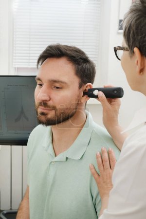 Photo for Man has appointment at clinic, checking hearing. Doctor audiologist consulting at hearing rehabilitation clinic to select digital device for middle age man. Doctor consulting patient - Royalty Free Image