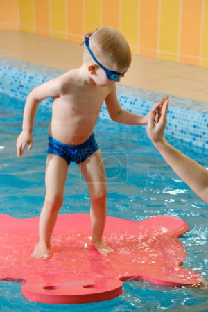 Téléchargez les photos : Enfant en bas âge apprenant à plonger dans la piscine intérieure avec professeur. Debout sur le côté, équilibre et activité physique générale pour les enfants dans l'eau, développement précoce. Garçon enfant instruit - en image libre de droit