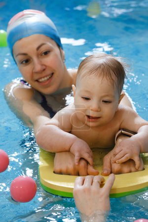 Photo for Early age swimming in pool. Baby boy trained to swim in water. Happy child with trainer woman in indoor swimming pool playing and having fun. Healthy and sport family with infant, active parent - Royalty Free Image