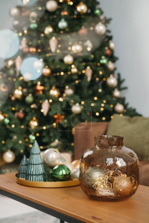 Foto de Decoración de Navidad en la mesa auxiliar sobre el fondo tradicional del árbol de Navidad. Sala de estar interior. Ajuste de mesa de Navidad sobre luces desenfocadas - Imagen libre de derechos