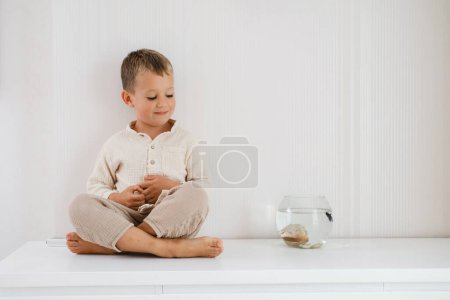 Foto de Chico mirando pecera. Lindo niño alimentando a los peces en el acuario en la mesa en casa - Imagen libre de derechos