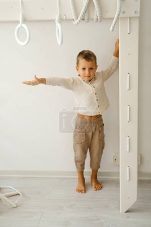 Téléchargez les photos : L'enfant fait de l'exercice sur Toddler Indoor Gym Playset. Il monte l'échelle dans la salle de jeux. Garçon passant du temps sur les escaliers du complexe sportif. Tout-petit jouant. - en image libre de droit